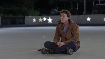 Movie still from “Serendipity” (2001), directed by Peter Chelsom – A man sitting on the ground in a parking lot; Medium shot, Over the shoulder angle