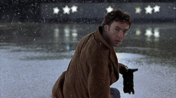 Movie still from “Serendipity” (2001), directed by Peter Chelsom – A man kneeling down in the snow holding a black cat; Medium shot, Low angle