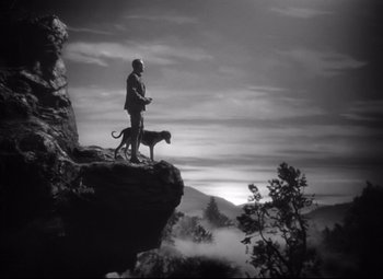 Movie still from “Sergeant York” (1941), directed by Howard Hawks – A man standing on top of a cliff with a dog; Wide shot, Low angle