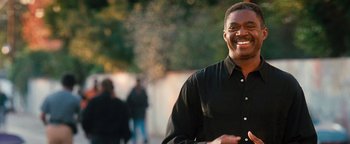 Movie still from “Set It Off” (1996), directed by F. Gary Gray – A man smiling for the camera while standing in front of a group of people; Close Up shot, Over the shoulder angle
