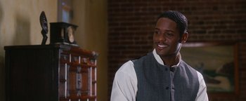 Movie still from “Set It Off” (1996), directed by F. Gary Gray – A young man smiles while standing in front of an antique chest; Close Up shot, Over the shoulder angle