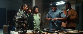 Movie still from “Set It Off” (1996), directed by F. Gary Gray – A group of people standing next to a table with guns on top of it; Medium shot, Over the shoulder angle
