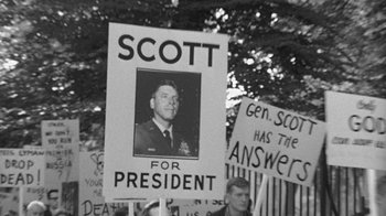 Movie still from “Seven Days in May” (1964), directed by John Frankenheimer – A sign with a picture of a man on it is shown; Medium shot, High angle
