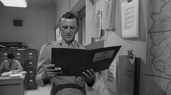 Movie still from “Seven Days in May” (1964), directed by John Frankenheimer – A man in a military uniform looking at a folder; Medium shot, Over the shoulder angle