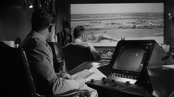 Movie still from “Seven Days in May” (1964), directed by John Frankenheimer – Two men are sitting in front of a large screen television; Wide shot, Low angle