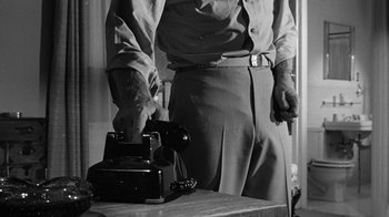 Movie still from “Seven Days in May” (1964), directed by John Frankenheimer – A man holding a knife standing in front of an old - fashioned phone; Medium shot, Low angle
