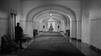 Movie still from “Seven Days in May” (1964), directed by John Frankenheimer – A person walking down a hall way in a building; Extreme Wide shot, Low angle