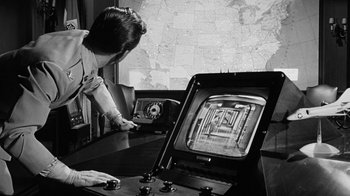 Movie still from “Seven Days in May” (1964), directed by John Frankenheimer – A man is standing in front of an old tv; Medium shot, High angle