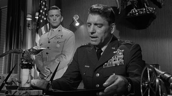 Movie still from “Seven Days in May” (1964), directed by John Frankenheimer – A man in a military uniform is standing in front of an american flag; Medium shot, Low angle