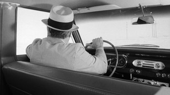 Movie still from “Seven Days in May” (1964), directed by John Frankenheimer – A man driving a car with a hat on; Medium shot, Over the shoulder angle