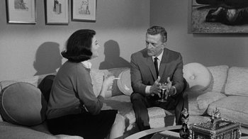 Movie still from “Seven Days in May” (1964), directed by John Frankenheimer – An older man and woman sitting on a couch talking; Medium shot, Over the shoulder angle