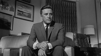 Movie still from “Seven Days in May” (1964), directed by John Frankenheimer – An older man in a suit sitting on a couch in a living room; Medium shot, Low angle