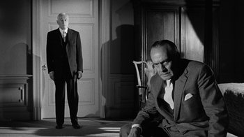 Movie still from “Seven Days in May” (1964), directed by John Frankenheimer – A man in a suit and tie next to another man in a suit and tie in front of an open door; Medium shot, Low angle