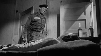 Movie still from “Seven Days in May” (1964), directed by John Frankenheimer – An old black and white photo of a man in a military uniform looking at a man lying on a couch; Medium shot, Over the shoulder angle