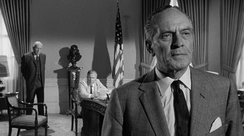 Movie still from “Seven Days in May” (1964), directed by John Frankenheimer – A man in a suit and tie in front of an american flag; Medium shot, Low angle