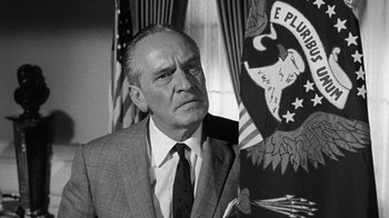 Movie still from “Seven Days in May” (1964), directed by John Frankenheimer – An older man wearing a suit and tie in front of an american flag; Close Up shot, Low angle