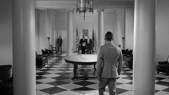 Movie still from “Seven Days in May” (1964), directed by John Frankenheimer – A man in a suit stands in front of two other men in suits; Wide shot, Over the shoulder angle