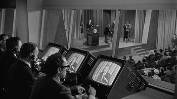 Movie still from “Seven Days in May” (1964), directed by John Frankenheimer – A man sitting in front of a television; Wide shot, High angle