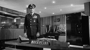 Movie still from “Seven Days in May” (1964), directed by John Frankenheimer – A man in a military uniform standing next to a reception desk; Wide shot, Low angle