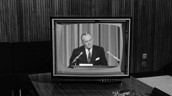 Movie still from “Seven Days in May” (1964), directed by John Frankenheimer – An old television with a man on the screen and microphones; Medium shot, Over the shoulder angle