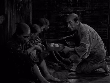 Movie still from “Seven Samurai” (1954), directed by Akira Kurosawa – An old man holding a tray of food in front of a group of young boys; Medium shot, High angle