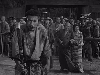 Movie still from “Seven Samurai” (1954), directed by Akira Kurosawa – Black and white photograph of a group of men and women in traditional garb; Medium shot, High angle