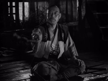 Movie still from “Seven Samurai” (1954), directed by Akira Kurosawa – A man sitting on the ground holding a sword; Medium shot, High angle