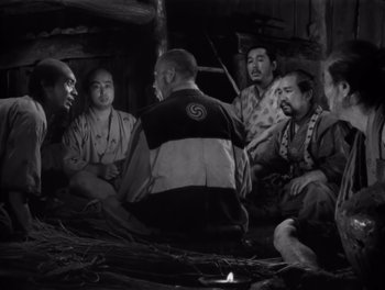 Movie still from “Seven Samurai” (1954), directed by Akira Kurosawa – A black and white photo of a group of men sitting in a circle; Medium shot, High angle