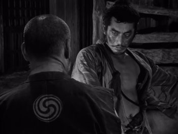 Movie still from “Seven Samurai” (1954), directed by Akira Kurosawa – A man in a black shirt is talking to another man in a black shirt; Medium shot, Over the shoulder angle