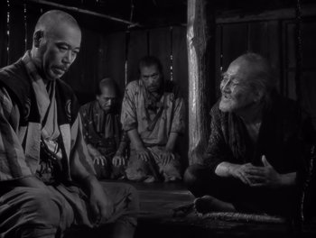 Movie still from “Seven Samurai” (1954), directed by Akira Kurosawa – A black and white photo of a group of people sitting around; Medium shot, Over the shoulder angle