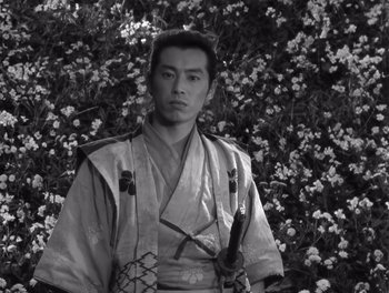Movie still from “Seven Samurai” (1954), directed by Akira Kurosawa – A man in a kimono standing in front of flowers; Medium shot, Low angle