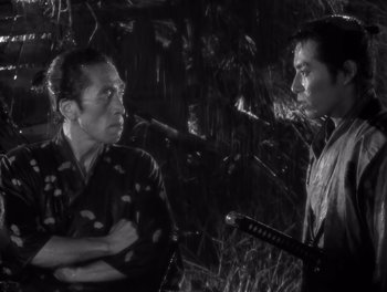Movie still from “Seven Samurai” (1954), directed by Akira Kurosawa – A man and a woman standing next to each other in front of trees; Medium shot, Low angle