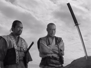 Movie still from “Seven Samurai” (1954), directed by Akira Kurosawa – Two men standing next to each other holding swords; Medium shot, Low angle