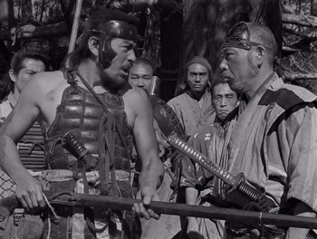 Movie still from “Seven Samurai” (1954), directed by Akira Kurosawa – A man in a samurai outfit holding a wooden sword; Medium shot, Over the shoulder angle
