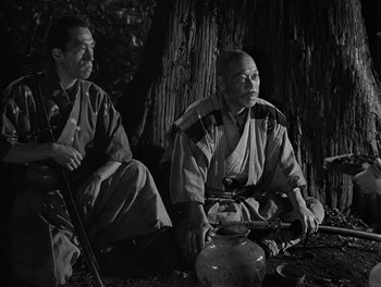 Movie still from “Seven Samurai” (1954), directed by Akira Kurosawa – Two men sitting next to each other in front of a tree; Medium shot, High angle