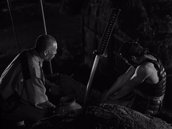 Movie still from “Seven Samurai” (1954), directed by Akira Kurosawa – Two men are working together in a cave; Medium shot, Low angle