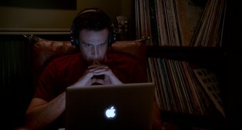 Movie still from “Sex Tape” (2014), directed by Jake Kasdan – A man wearing headphones and sitting in front of an open laptop computer; Medium shot, High angle