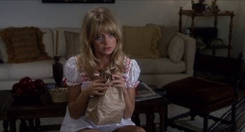 Movie still from “Shampoo” (1975), directed by Hal Ashby – A woman sitting on the ground holding a bag of food; Medium shot, High angle