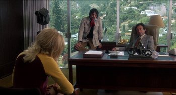 Movie still from “Shampoo” (1975), directed by Hal Ashby – A man sitting at a desk in front of two women; Wide shot, Over the shoulder angle