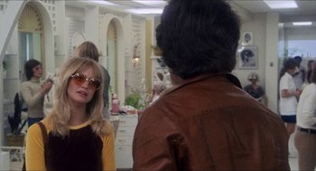Movie still from “Shampoo” (1975), directed by Hal Ashby – A woman wearing sunglasses and a brown leather jacket talking to a man in front of a mirror; Medium shot, Over the shoulder angle
