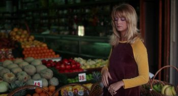 Movie still from “Shampoo” (1975), directed by Hal Ashby – A woman standing in front of a display of fruits; Medium shot, High angle