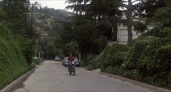 Movie still from “Shampoo” (1975), directed by Hal Ashby – A man riding a motorcycle down the middle of a street; Extreme Wide shot, High angle