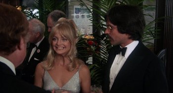 Movie still from “Shampoo” (1975), directed by Hal Ashby – A man and a woman are smiling for the camera; Medium shot, Over the shoulder angle