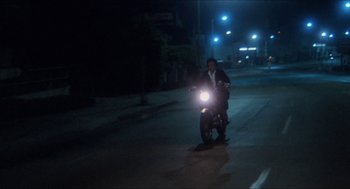 Movie still from “Shampoo” (1975), directed by Hal Ashby – A man riding a motorcycle down a street at night; Wide shot, Low angle