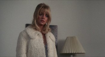 Movie still from “Shampoo” (1975), directed by Hal Ashby – A woman in a white coat standing in front of a lamp; Close Up shot, Over the shoulder angle