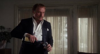 Movie still from “Shampoo” (1975), directed by Hal Ashby – A man in a suit and tie holding a bottle of wine; Medium shot, Low angle