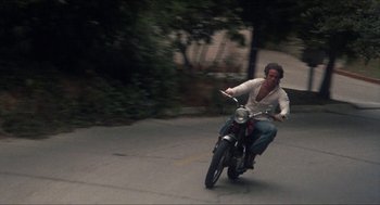Movie still from “Shampoo” (1975), directed by Hal Ashby – A man riding a motorcycle down a street; Wide shot, Low angle