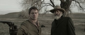 Movie still from “Godless” (2017), directed by Scott Frank – A man and a man in a hat standing next to each other; Close Up shot, Over the shoulder angle