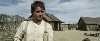 Movie still from “Godless” (2017), directed by Scott Frank – A man standing in front of a wooden house; Close Up shot, Over the shoulder angle