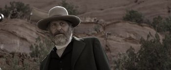 Movie still from “Godless” (2017), directed by Scott Frank – A man with a beard and a hat in a field; Close Up shot, Low angle